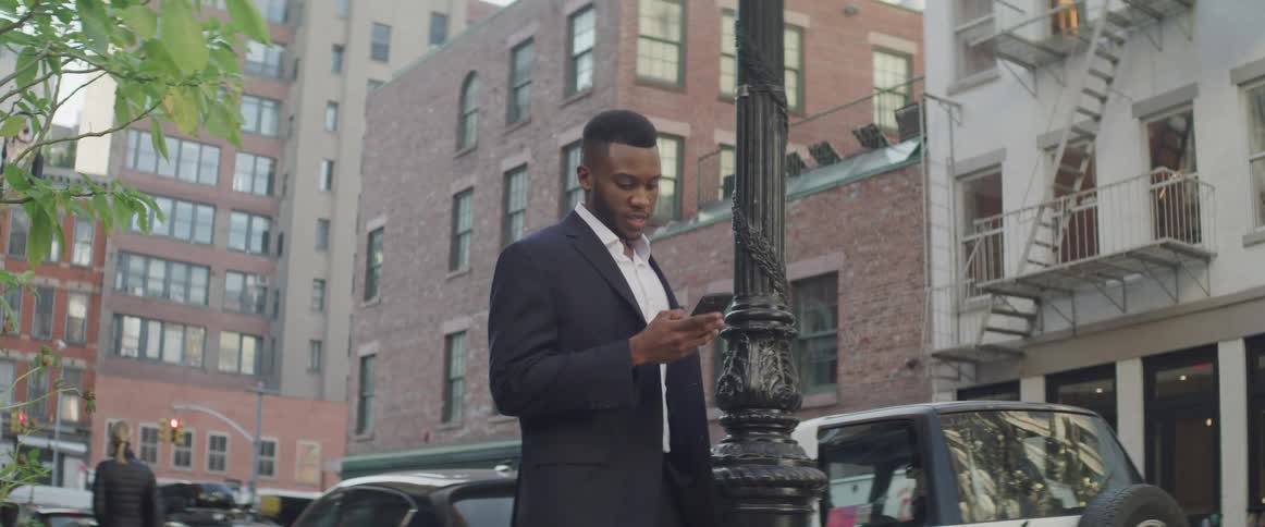 A man looks at his cell phone standing on a city sidewalk