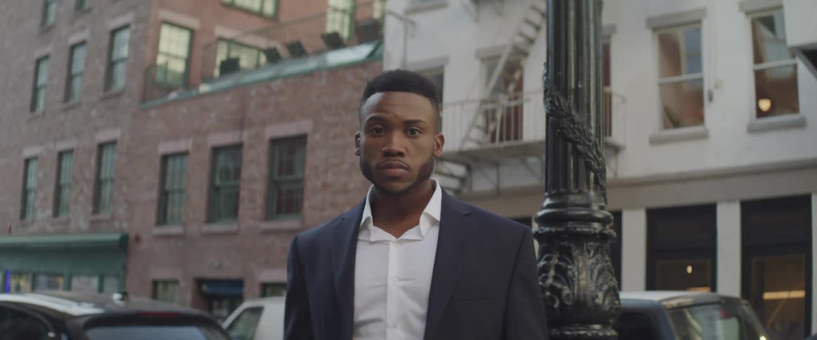 Black businessman looking sideways turns his head to the camera in the street