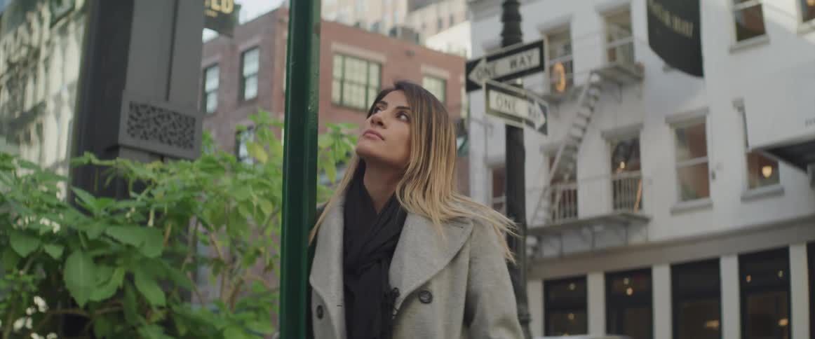 A woman leans against a pole in a neighborhood