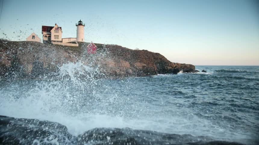 Waves are crashing against the shore near a lighthouse