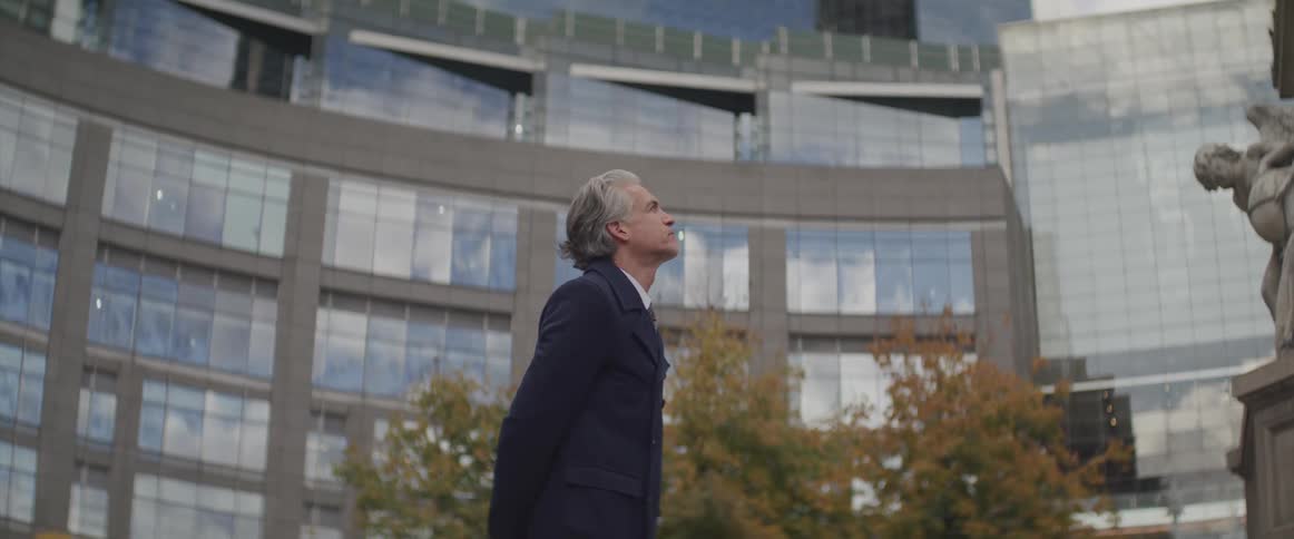 Businessman stands and looks at the statue in the city square