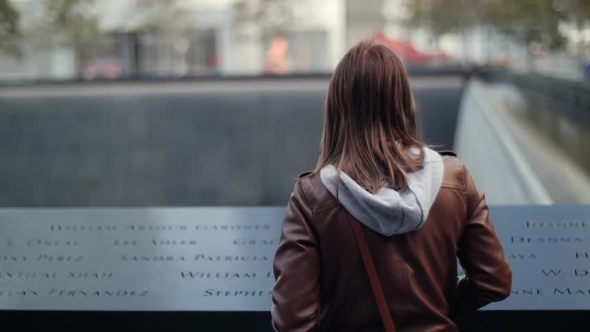 A woman stands looking at names on a monument in the daytime