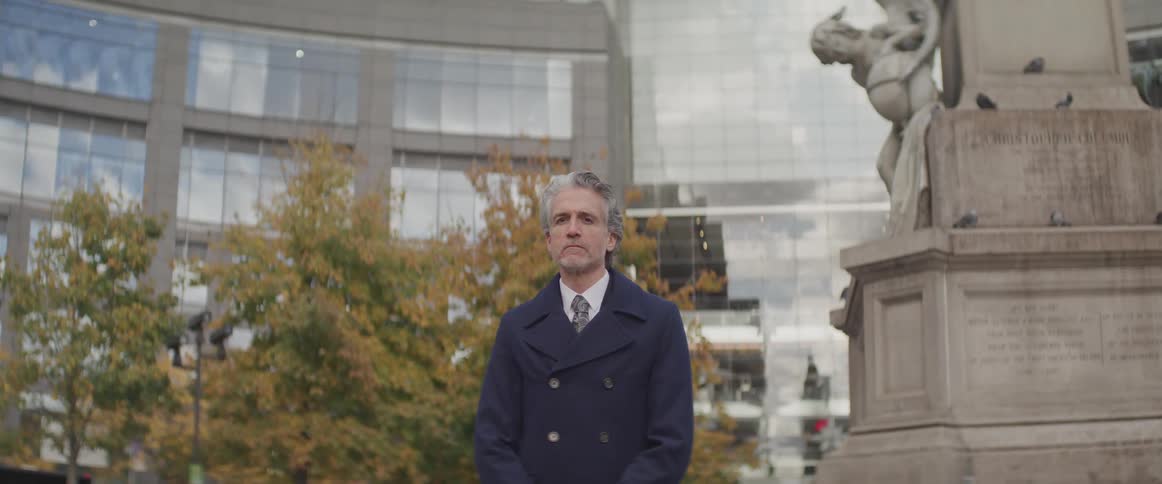 Businessman stands next to the statue and in front of the buildings