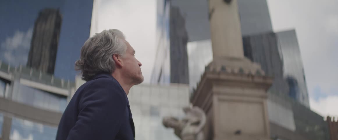 Businessman stands and looks up at the sky next to the office buildings