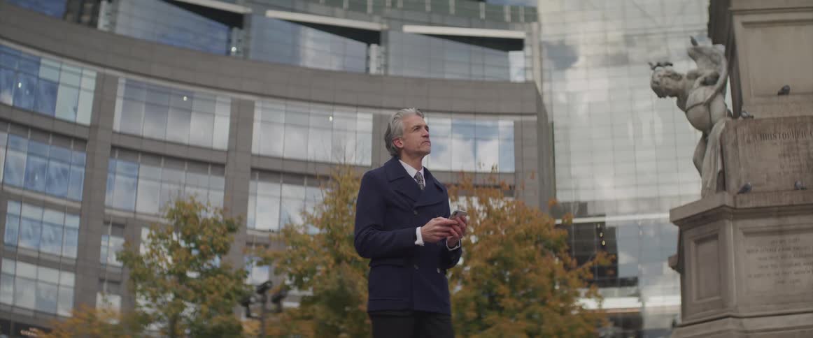 Businessman stands and uses a smartphone next to the statue in front of the office buildings