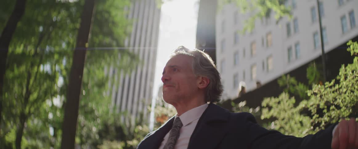 Business man sits on the bench while the sun shines brightly in the public park