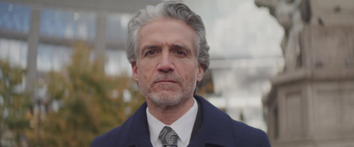 Businessman stands and turns his head to the camera next to the statue in front of the office buildings