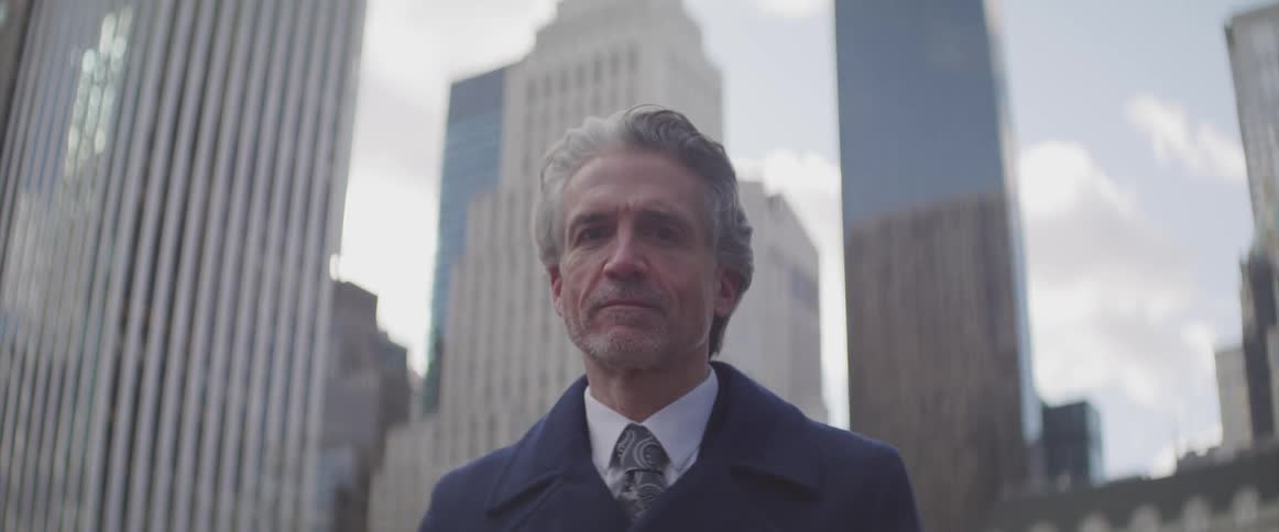 A man with a suit and a tie staring with buildings in the background
