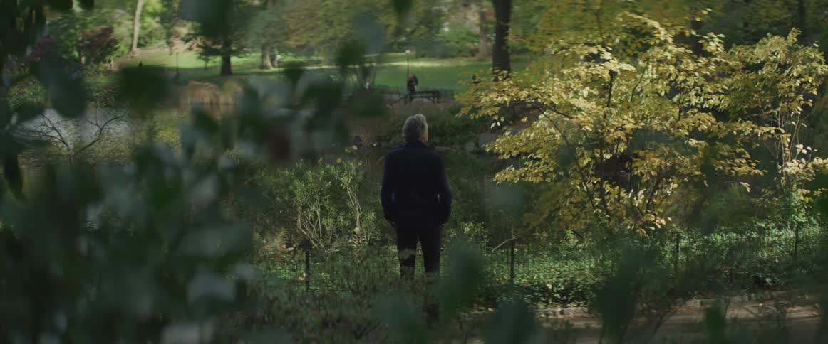 Man stands outdoors near fenced off water looking toward park