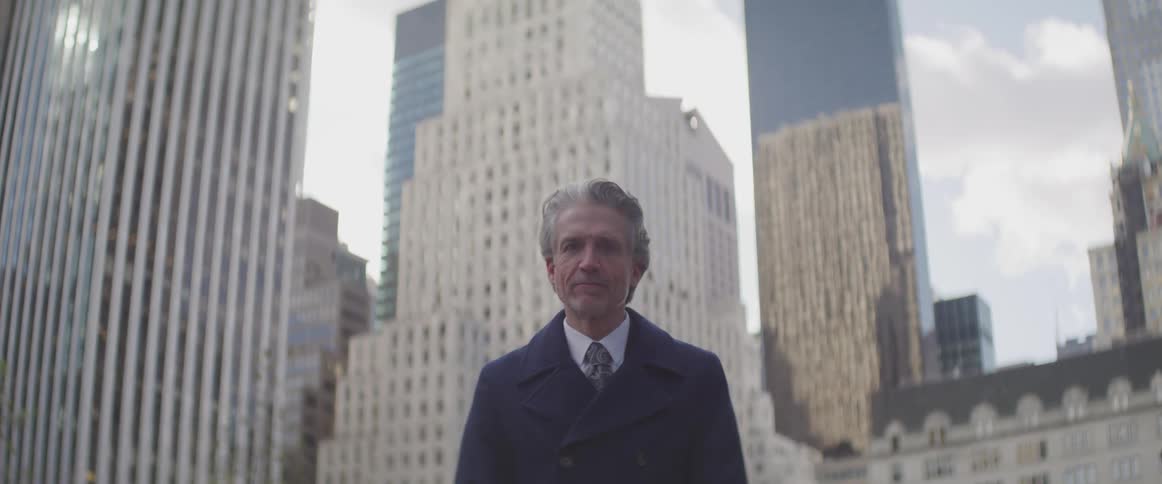 Businessman stands and raises his head in front of the tall office buildings