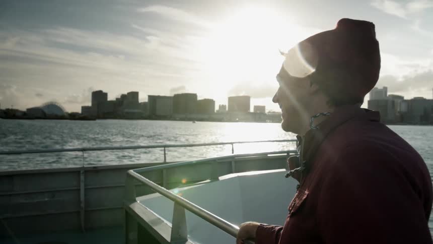 A man rides on a boat with city buildings in the background