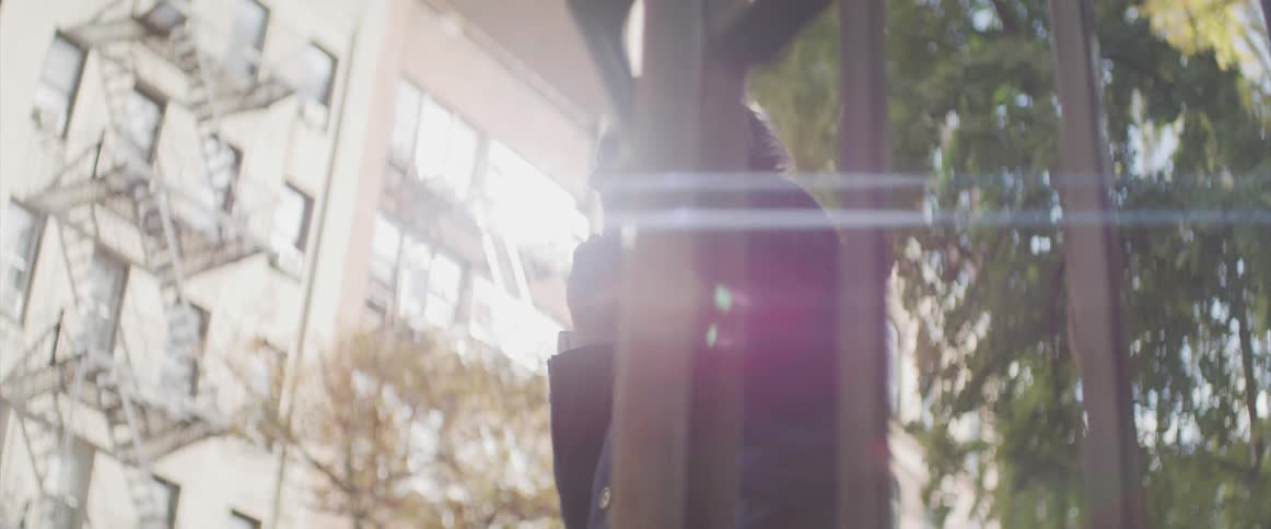 Male standing outside in a city neighborhoos in front of an aparment building holding a cell phone up to his ear