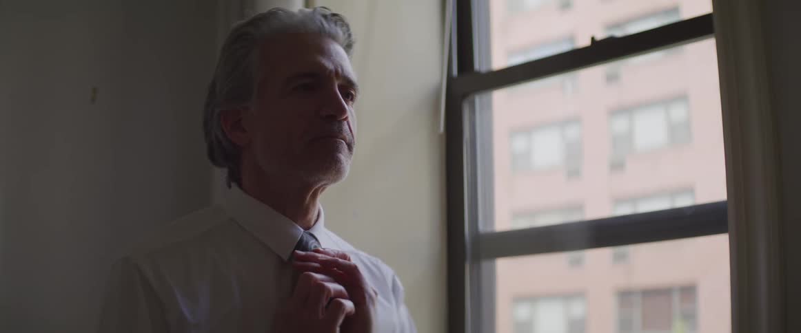Male stands next to a window adjusting and smoothing his tie