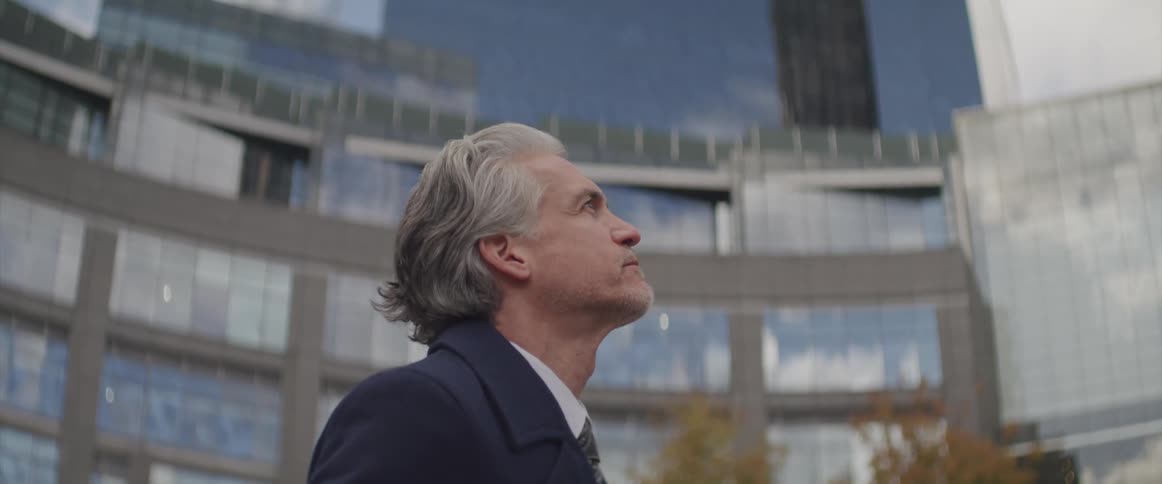 Businessman wearing a suit looks up at the tall office buildings