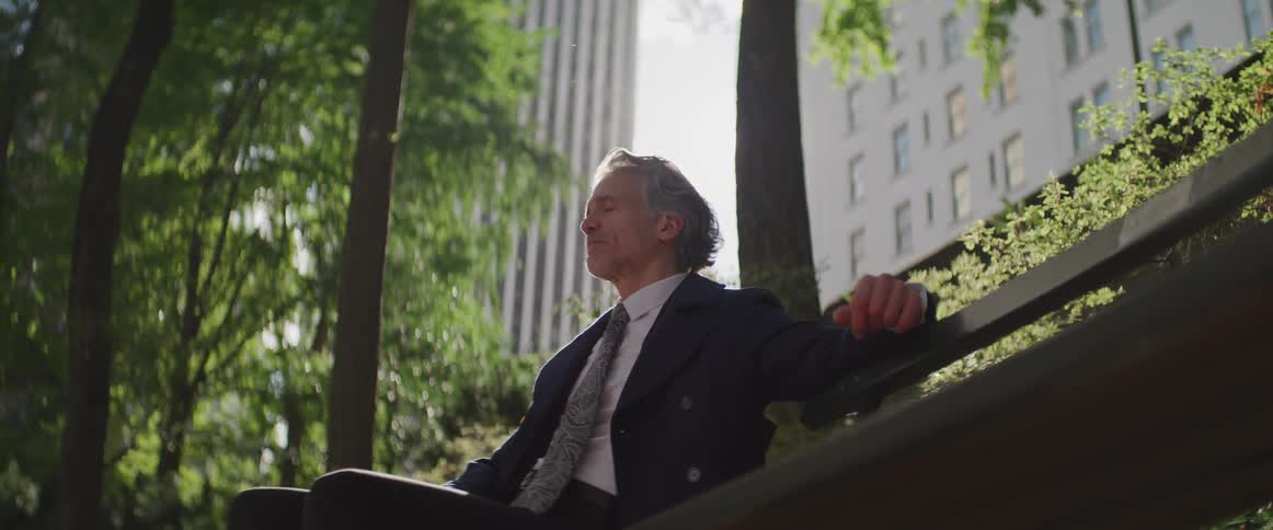 A man is resting on the bench outside of the building