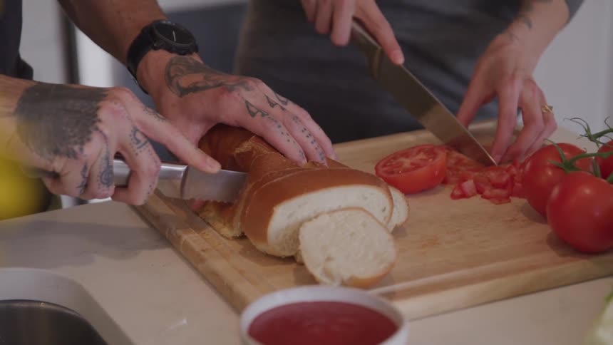 A man and woman cut bread and tomatoes at home