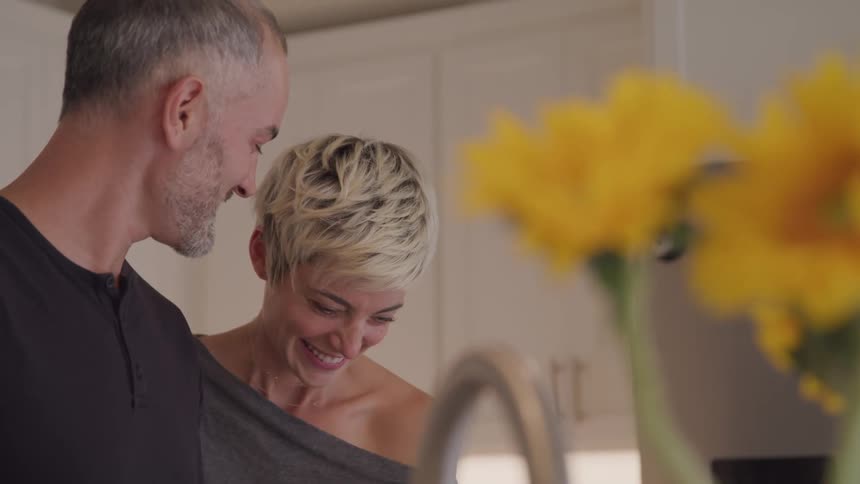 A man and woman laugh together in the kitchen