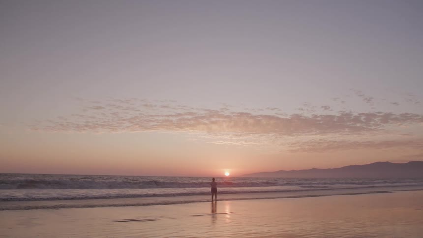 Man stands and watches sunset on the beach next to the sea