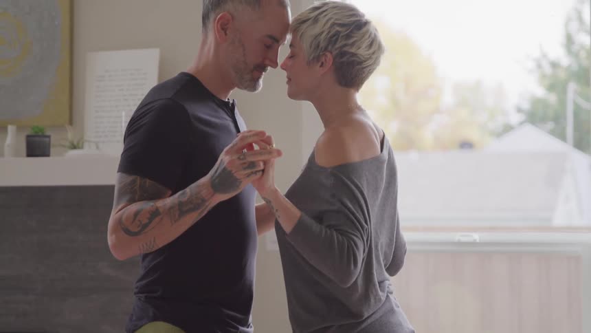 A husband and wife hold hands in the living room
