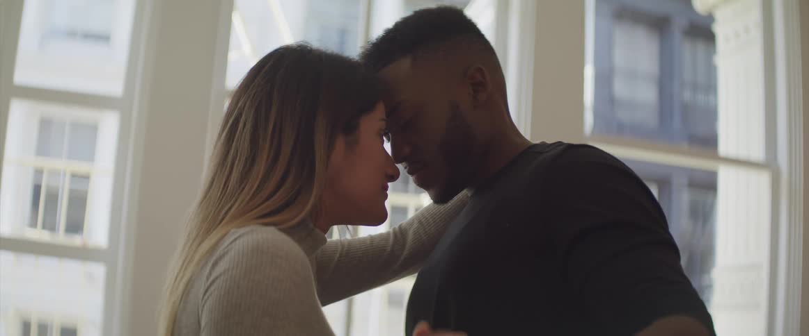Black man and brunette woman dance in the living room at home