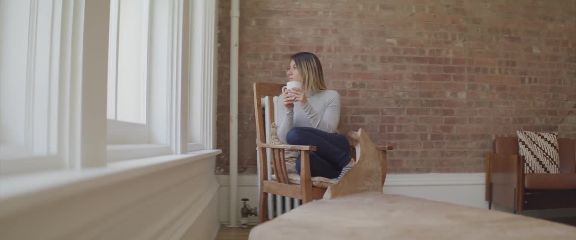 A woman sits with a drink by the window