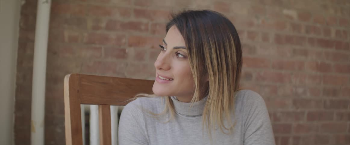 Blonde woman sits near a brick wall and looks over to her right