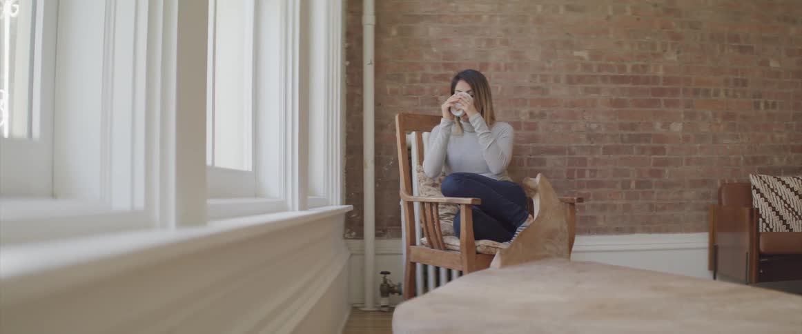A woman is drinking from a mug by the window