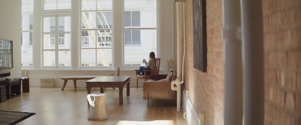 Woman sitting in the chair looks out the window in the living room