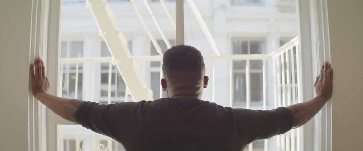 A black man stands and looks out a window