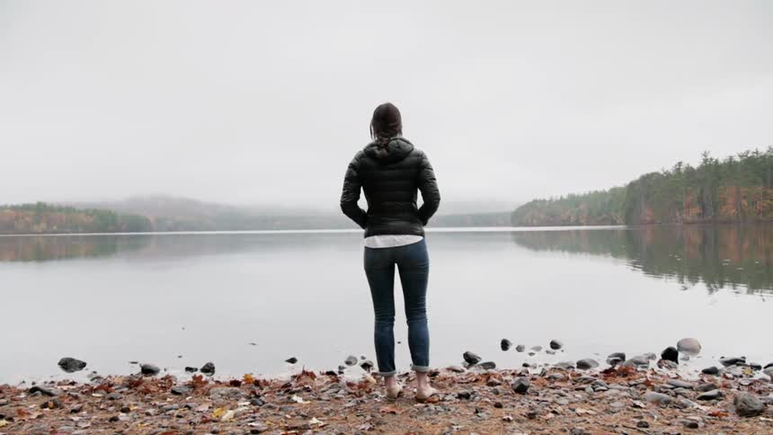 A woman standing on a rocky shoreline next to a lake