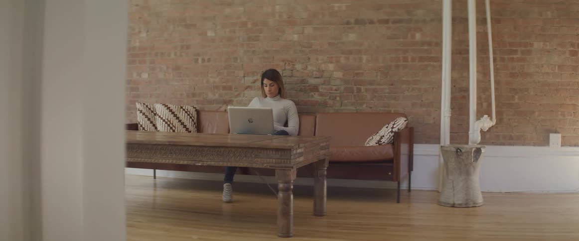 A woman sits on a couch and works on a laptop