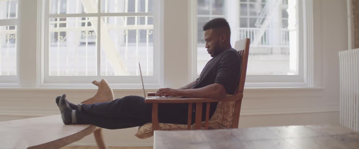 A man sits in a chair working on a laptop