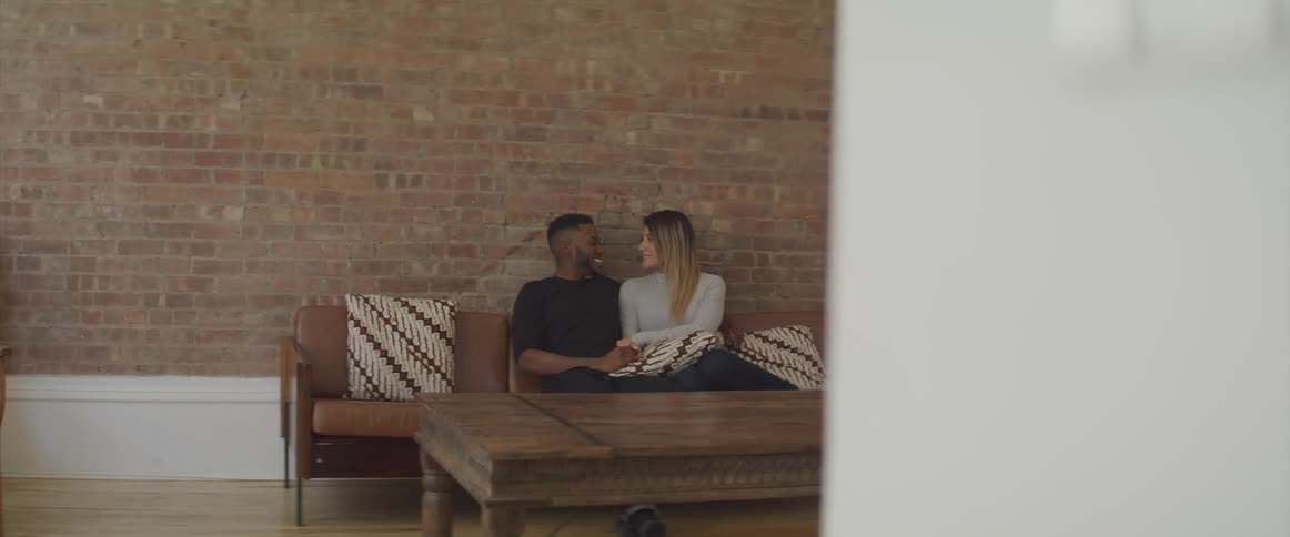 A couple cuddles on the leather sofa smiling and gazing at each other