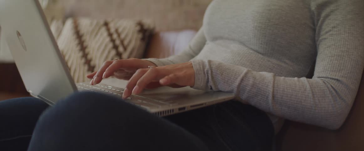 Close up of a woman typing on a laptop while relaxing on the couch