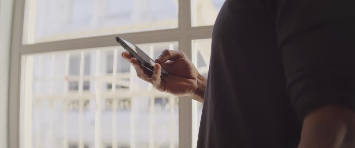 Black man touches his smartphone in a room
