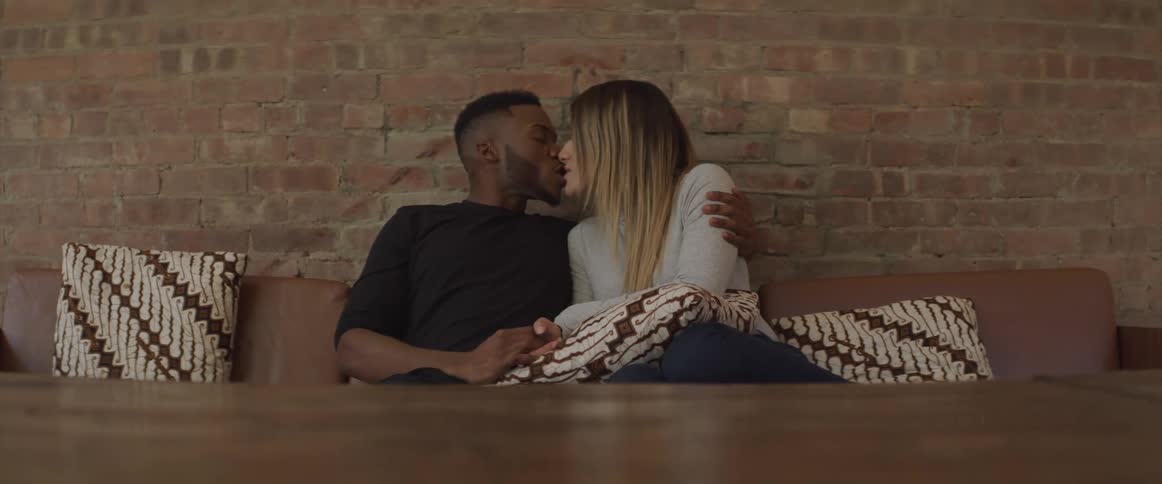 A man and a woman sitting on a couch kissing