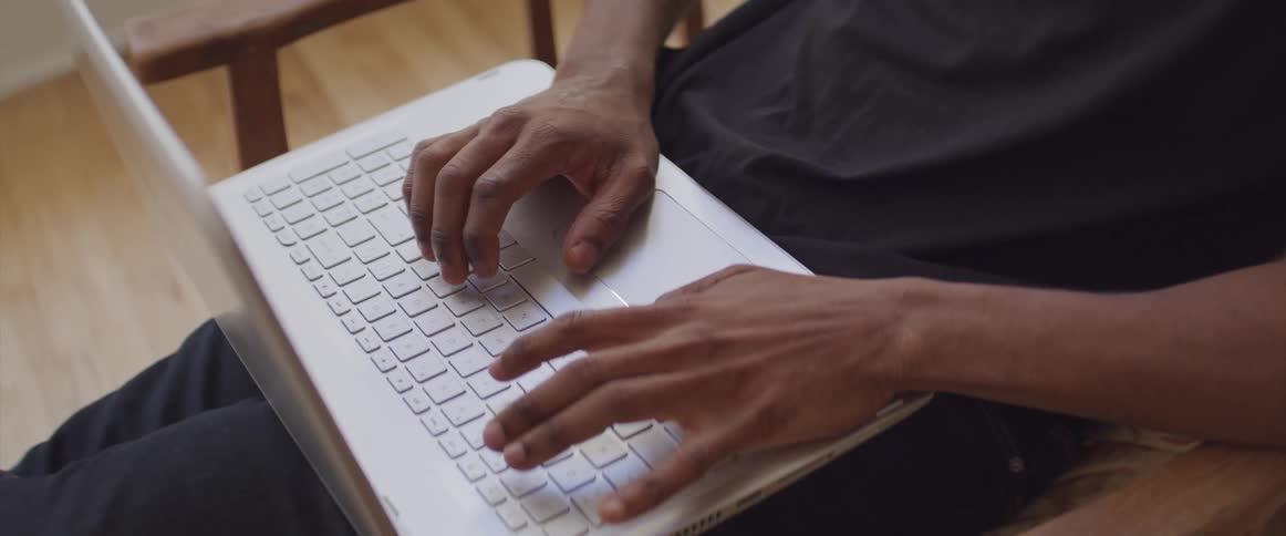 A man sits in a chair and types on a laptop in his lap