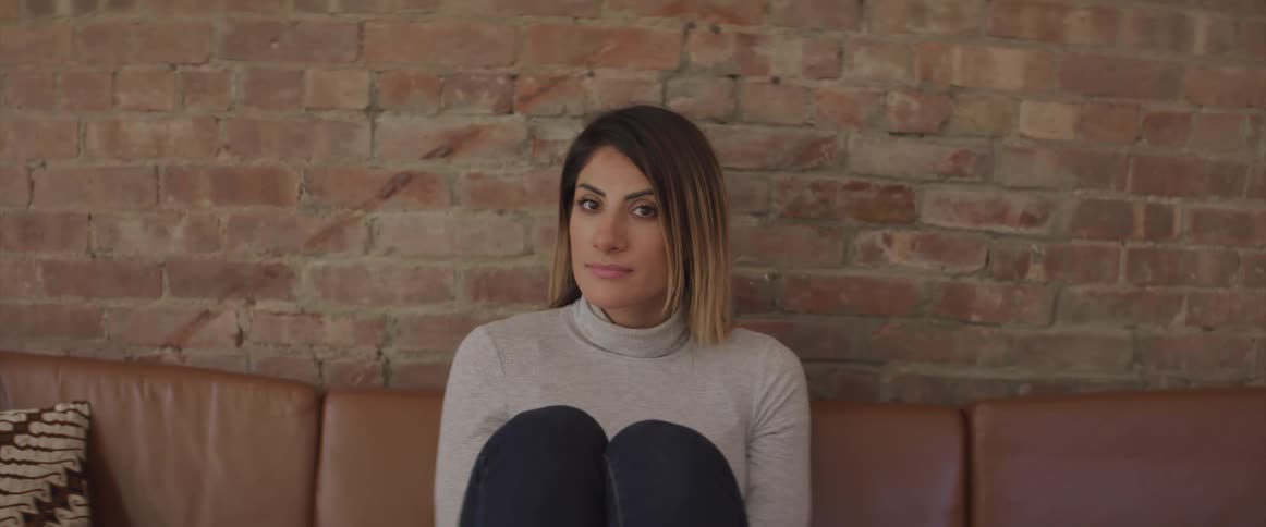 A woman sits on a couch with her knees up and looks around