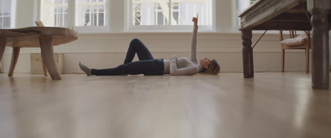 A woman lays on the floor and holds one arm up in the air