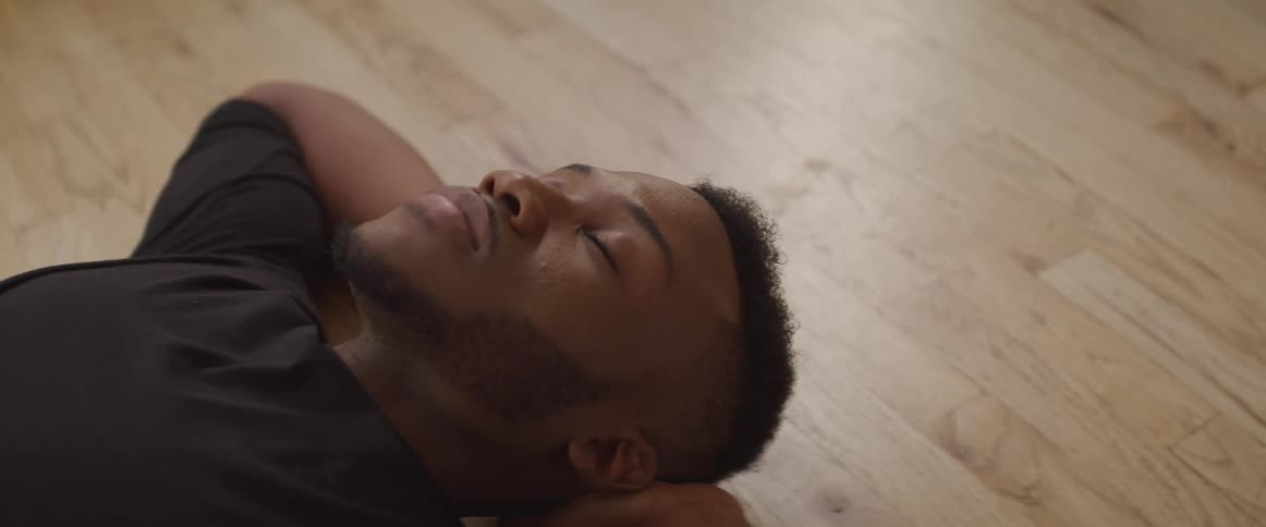 A man is lying on a wooden floor with his eyes closed