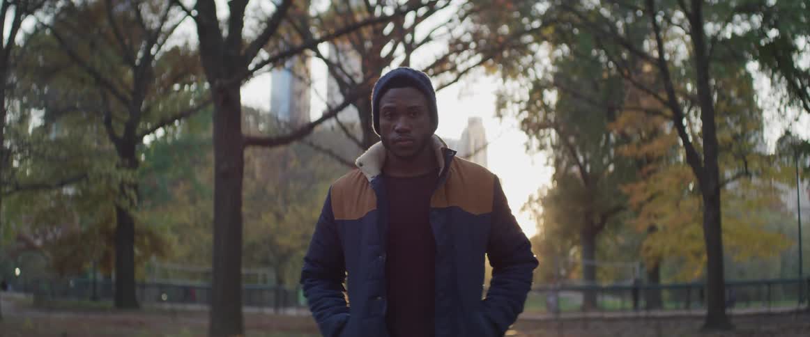 Black man stands and looks at the camera at sunset in the public park