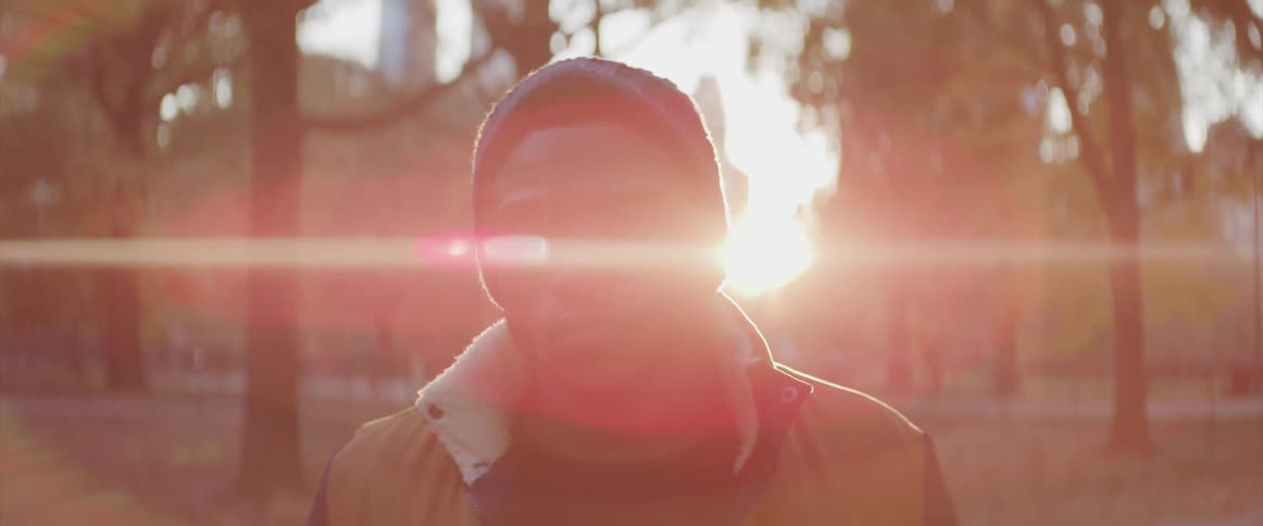 Black man stands and stares at the camera in the public park at sunset