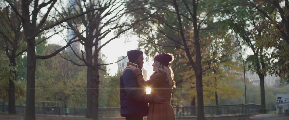 Young couple hughs in the park on the city at sunset