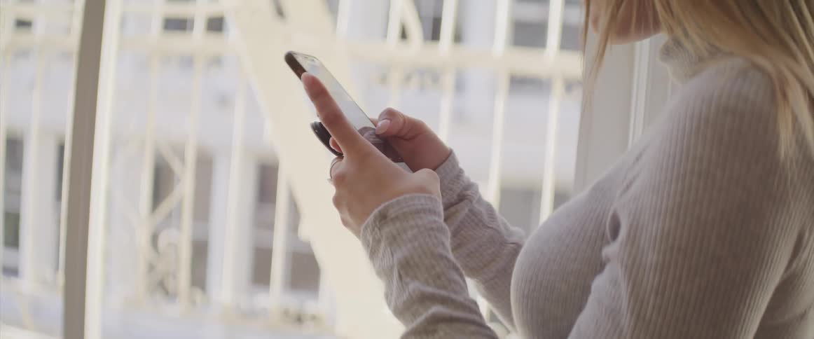 A woman using a smartphone while standing indoors near a window