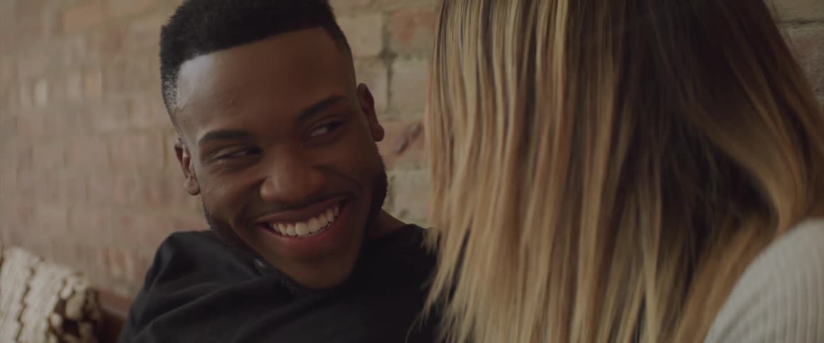 Black man and white woman sitting on the sofa talk to each other and laugh