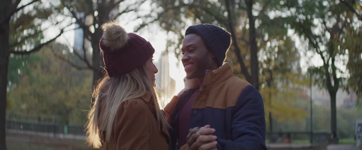Black man and white woman dance in the public park at dusk