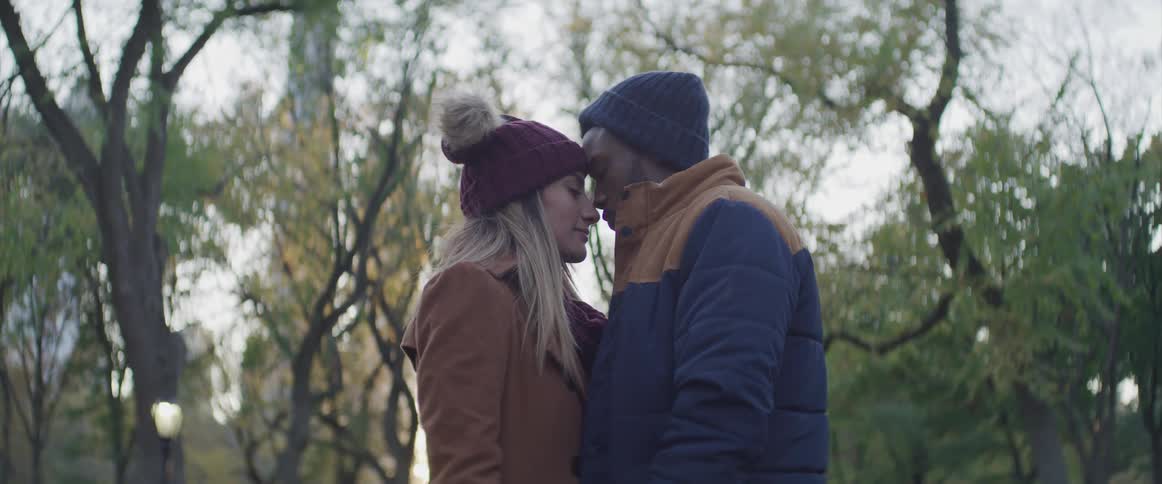 Young couple stand close to each other in a park at sunset