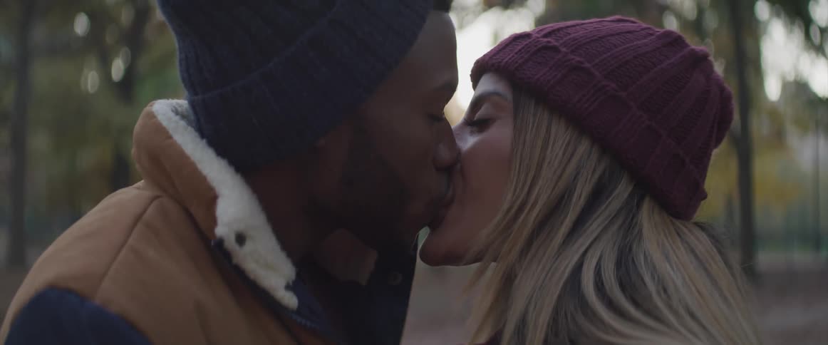 Black man and white woman kiss each other in the public park
