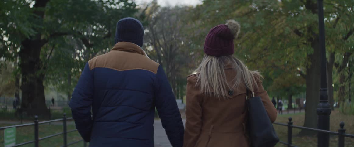 Black man and white woman holding hands walk in the public park