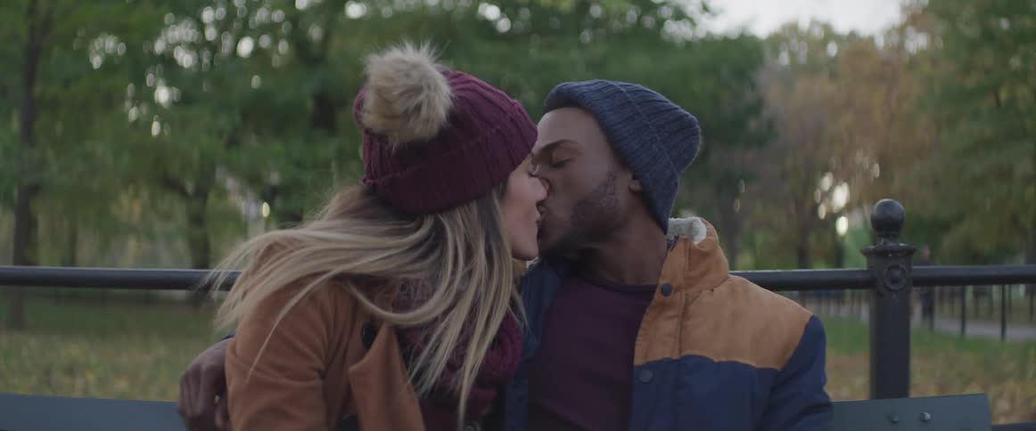 A man and woman kiss on the park bench